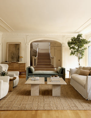The Elvie moss green velvet chaise sits in front of two marble coffee tables atop a jute rug with a grid pattern