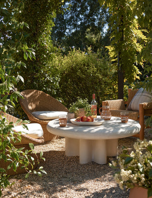 Ruiz round cement outdoor coffee table styled with wicker accent chairs in an outdoor lounge space.