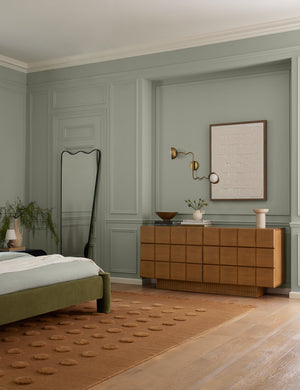 Kukka modern wavy adjustable two arm wall sconce in brass hung above a dresser in a bedroom