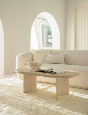 Charlotte oyster white lumbar velvet pillow sits on a cream sofa behind a light wooden oval coffee table