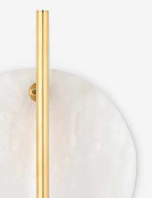 Angled close-up of the largest alabaster disc and brass pole in the middle of the Eleir sconce with antique brass finish