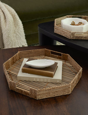 The woven geometric bamboo murai trays sit in a living room atop nested coffee tables with decorative bowls and books stacked within them
