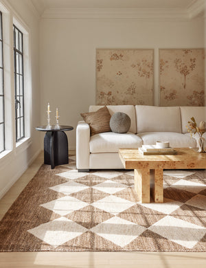 Cera Beeswax Column Candles in white sit in two glass candle holders in a living room with a cream couch and a rug with a diamond pattern
