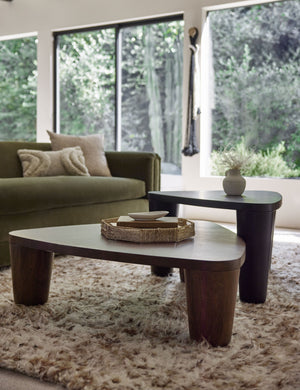 One woven geometric bamboo murai tray sits in a living room atop nested coffee tables with a green velvet sofa and a brown and white plush rug
