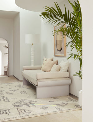 The Nabu white metal floor lamp with ribbed base and gold accents by Regina Andrew sits in the corner of an entry way with a plush geometric rug, a beige linen sofa, and a natural toned wall art